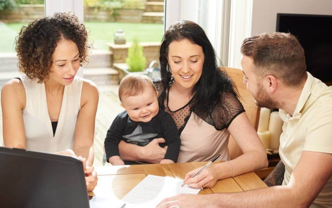 Madre firma un contrato de guardería mientras su bebé, su marido y su empleada de guardería observan.