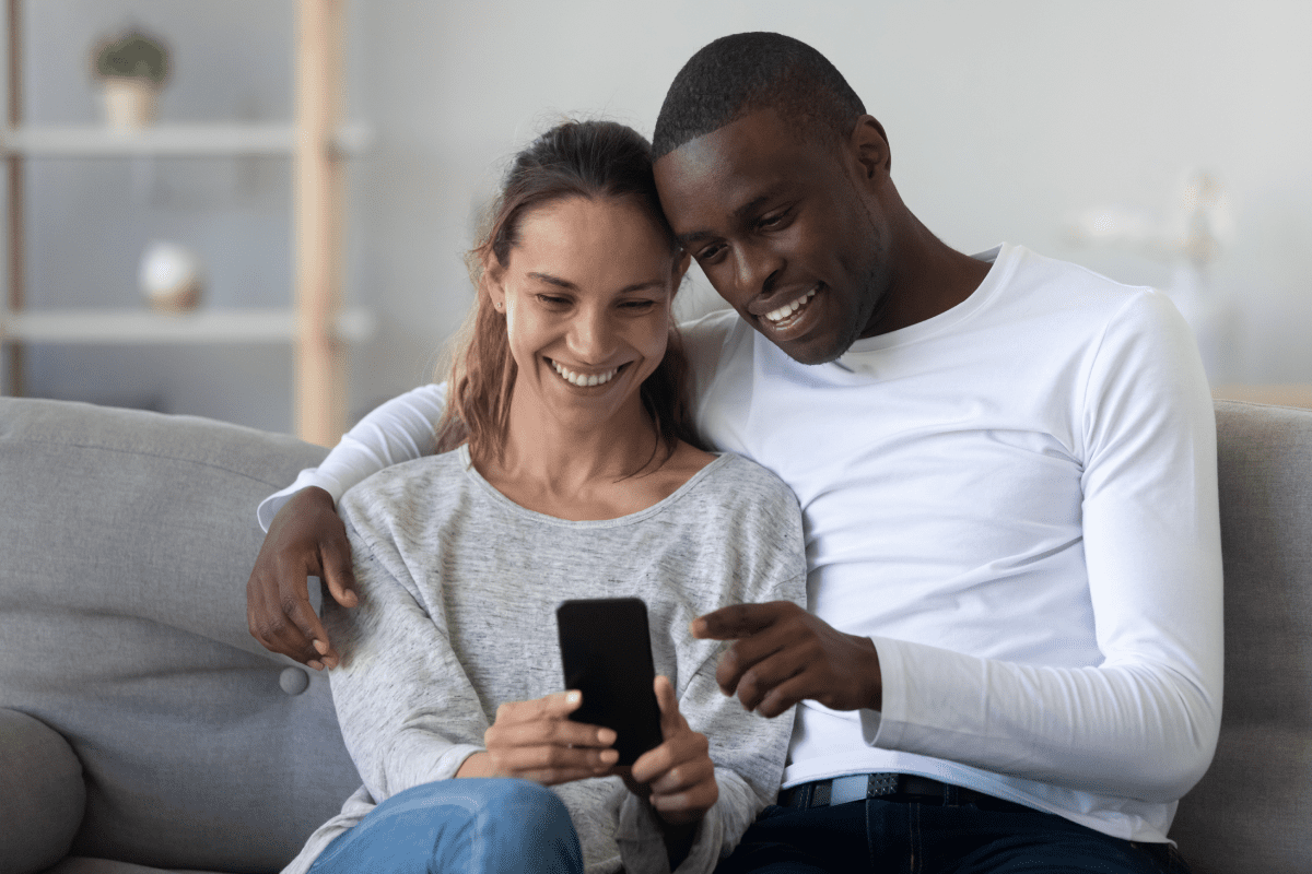 Happy couple sitting on a sofa and looking at prenuptial agreement on a smartphone