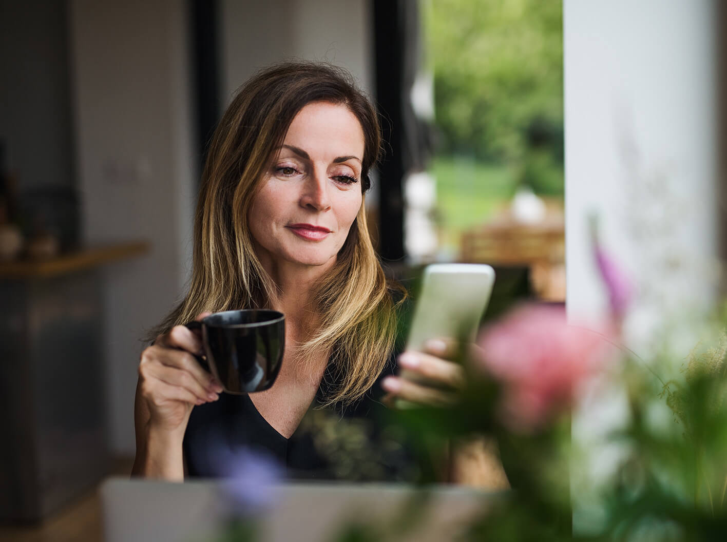 Woman looking at her phone while holding a beverage mug.