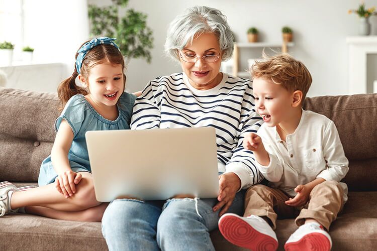 Grandmother with granddaughter and grandson looking at a laptop while seated on a sofa.