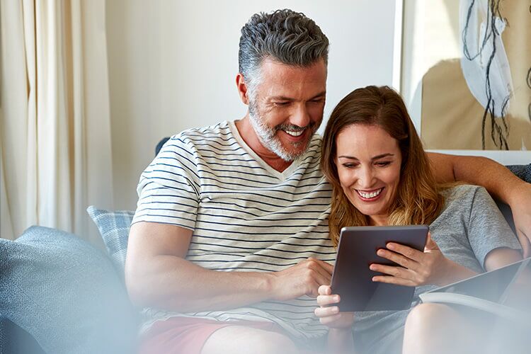 A man and a woman cuddle while looking at a tablet