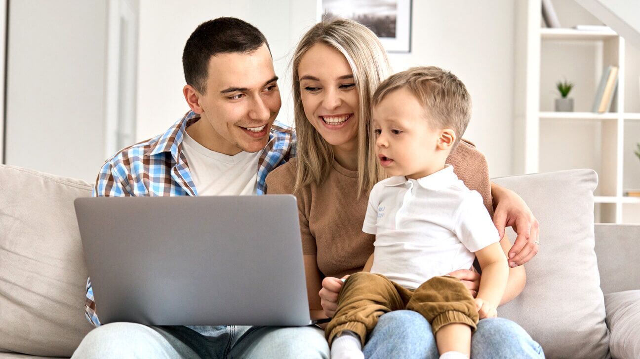 Mother, father and young son sitting on a couch and looking at a laptop screen.