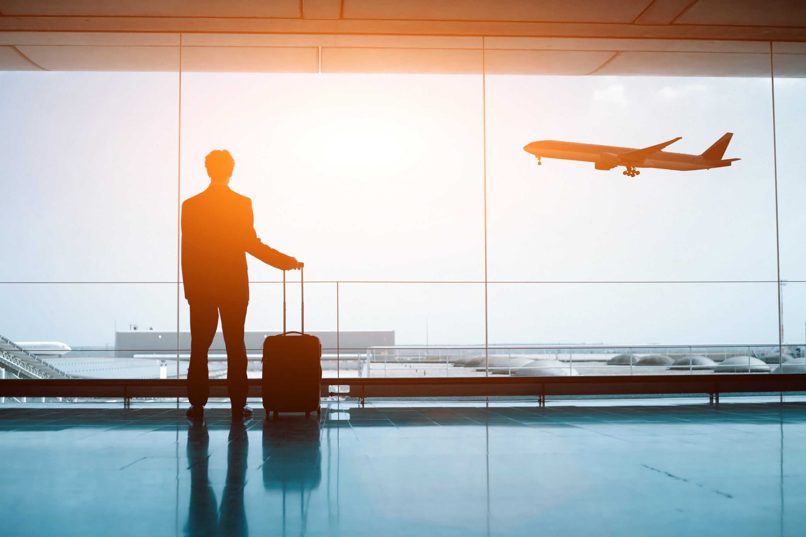 Man with luggage looking out airport window at jet taking off