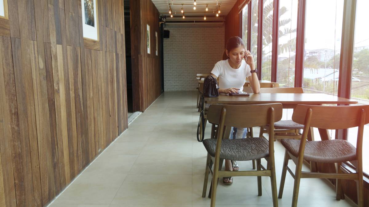 Mujer sentada en una mesa mientras habla por su teléfono celular y mira una tableta de computadora.