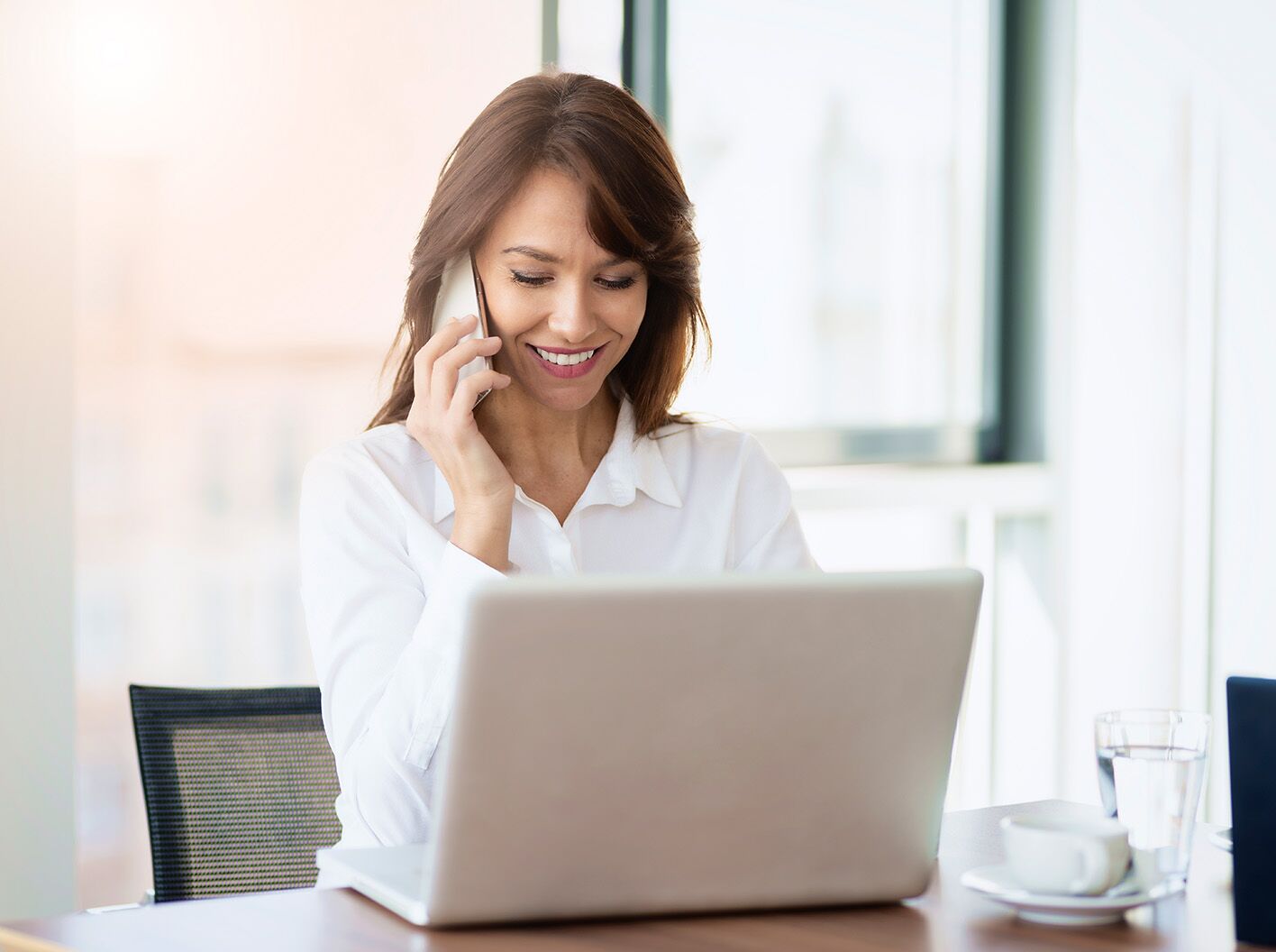 Woman talking on phone and looking at her laptop.