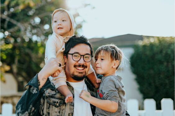 Un padre con sus dos hijos pequeños en brazos.