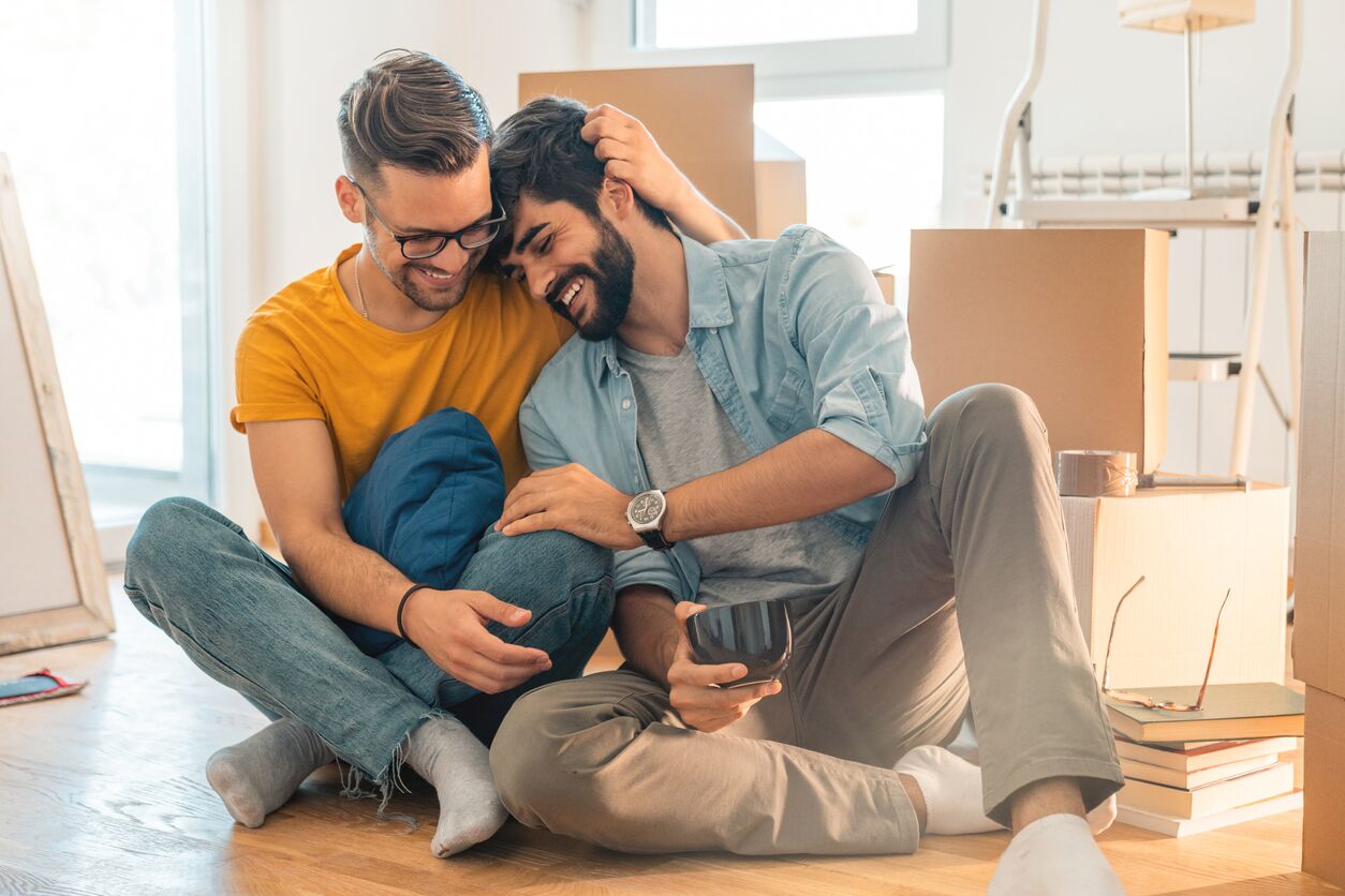 Pareja masculina sentada en el suelo y disfrutando de un nuevo hogar