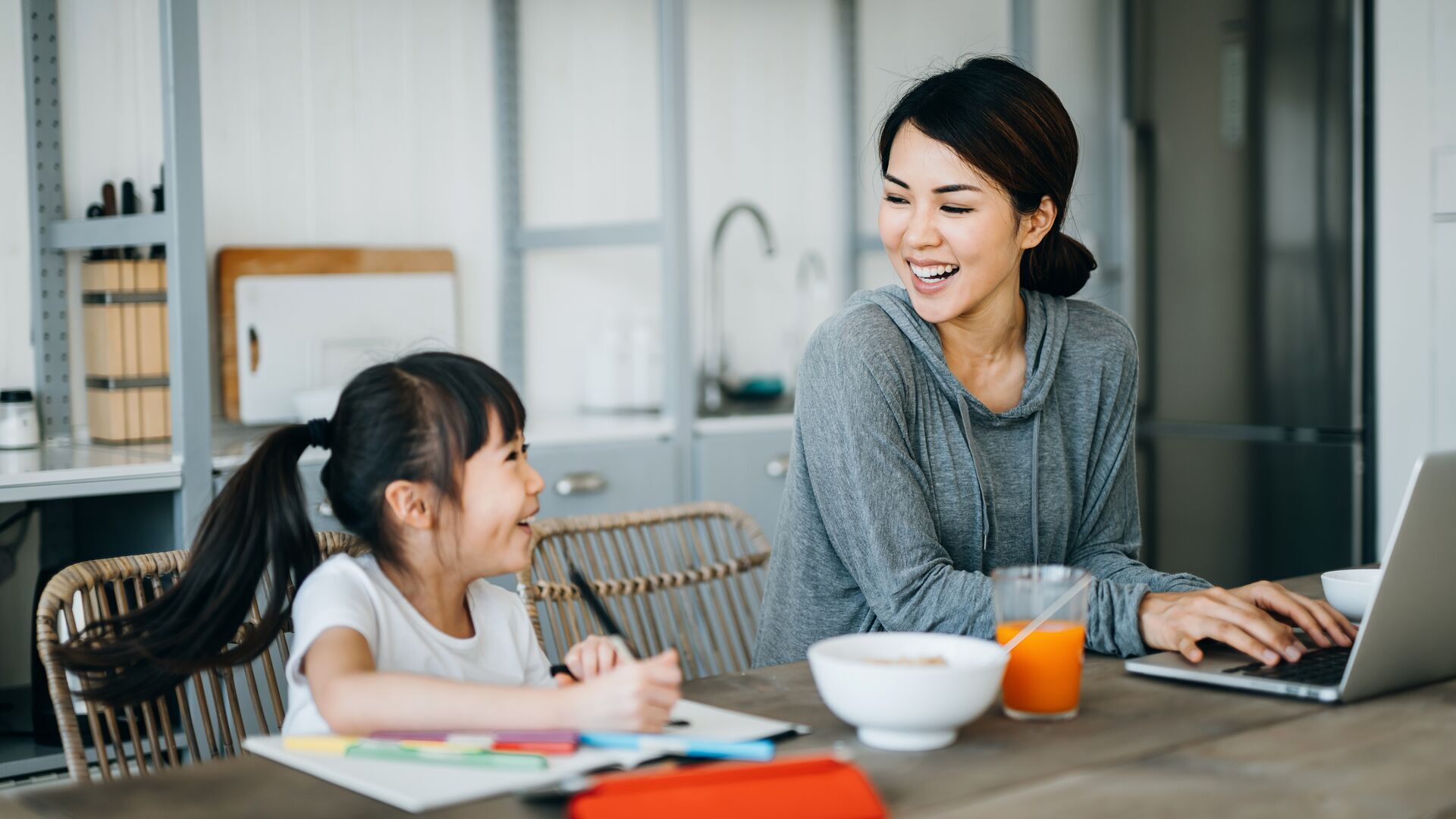 Mom typing on laptop and daughter coloring at kitchen table