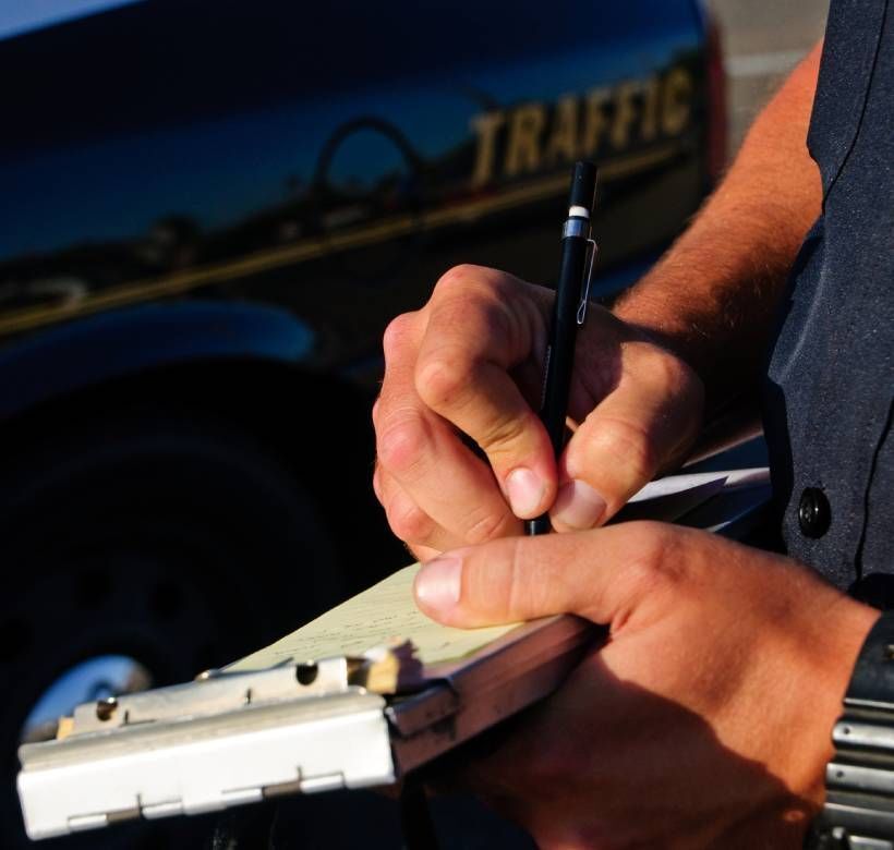 Traffic police officer writing a traffic moving violation ticket as he stands next to his patrol vehicle.