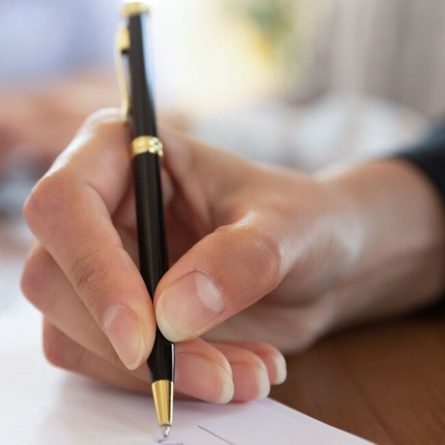 Primer plano de una mujer utilizando un bolígrafo de tinta para firmar y documentar.