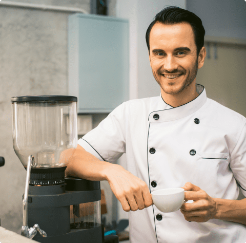 Un chef tomando café junto a una cafetera.