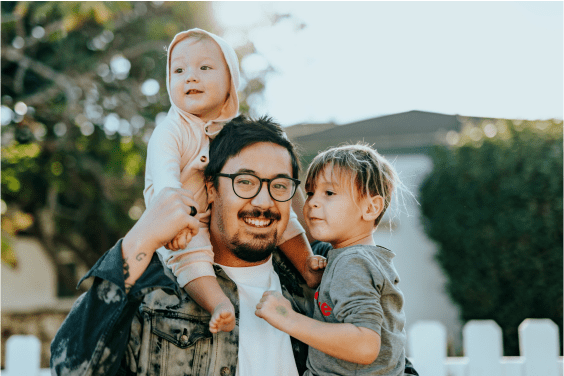 Un hombre sonriente con dos niños pequeños en el patio de su casa.