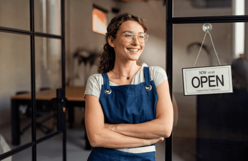 Una sonriente propietaria de una pequeña empresa frente a su tienda.