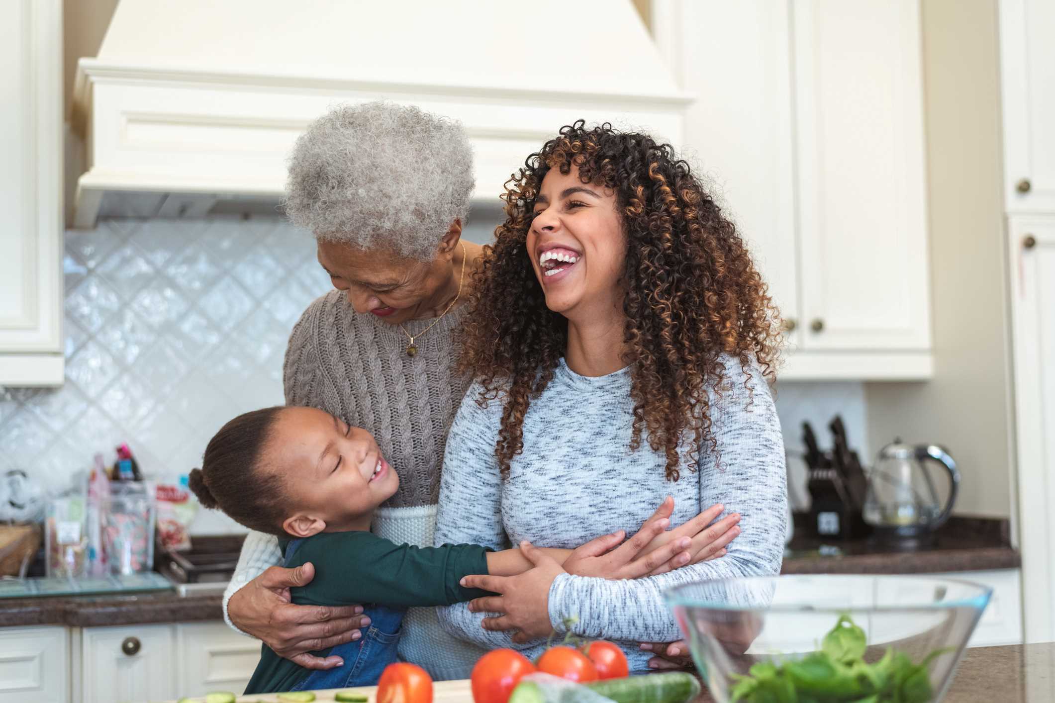 Grandmother, daughter and granddaughter embracing in kitchen while preparing a salad