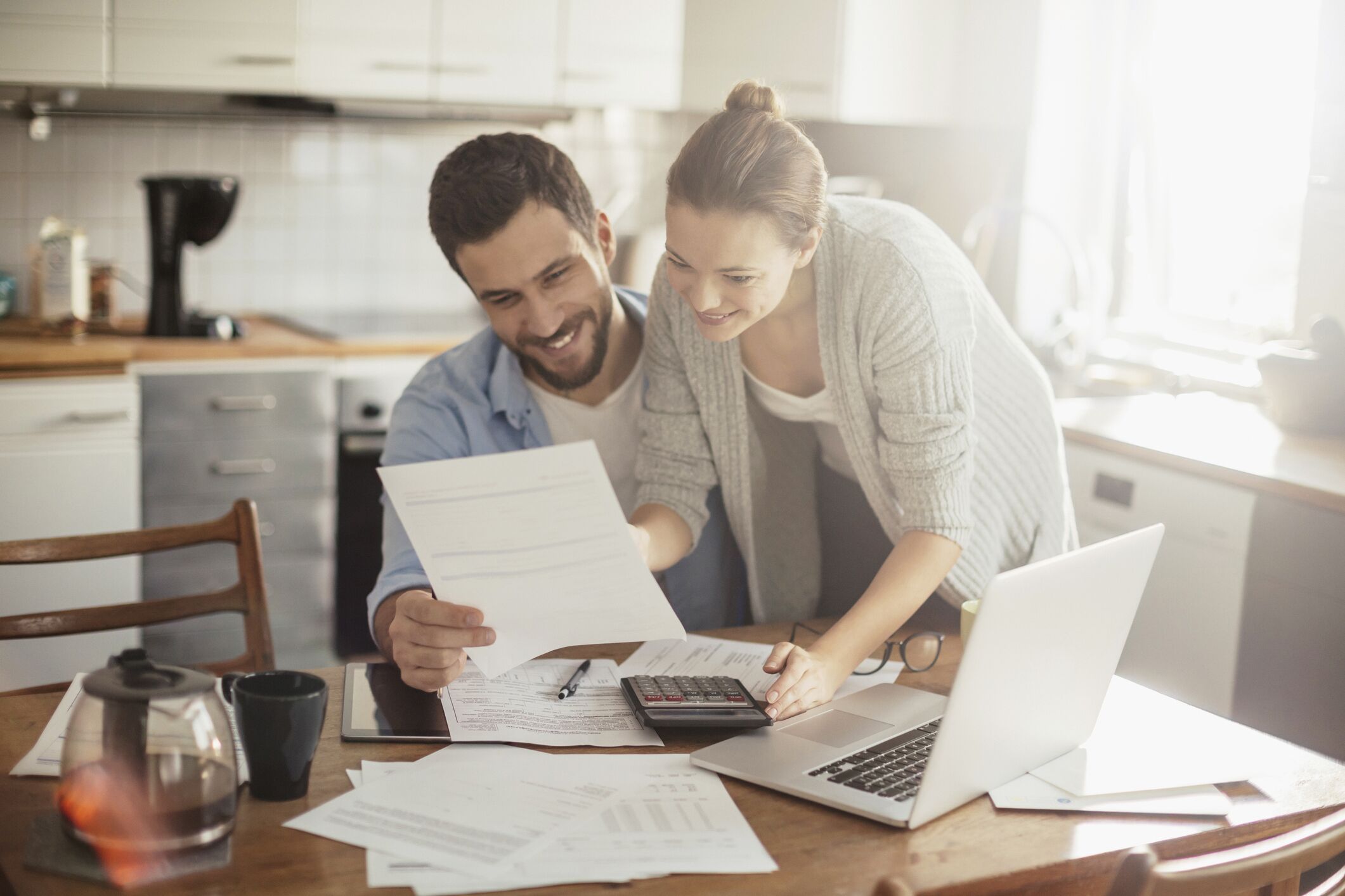 Young couple smiling and reviewing financial documents at their kitchen table