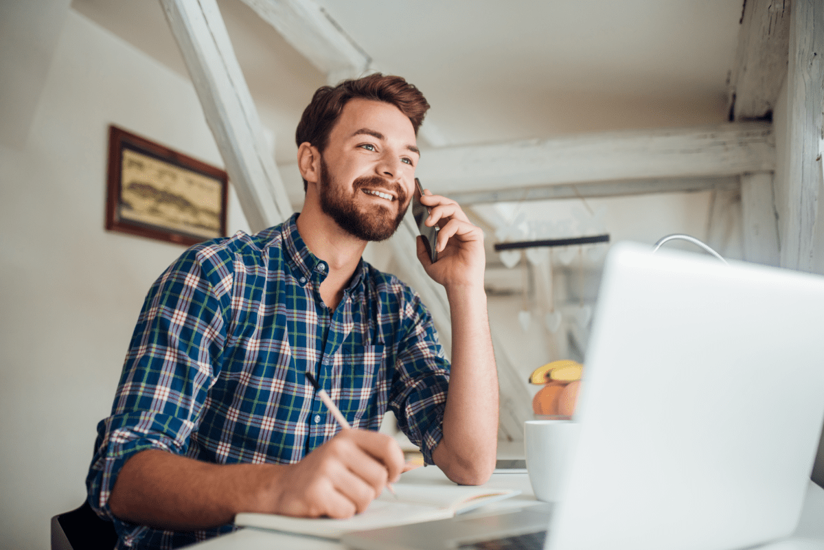 Smiling man working and talking on a cell phone in a casual workspace.