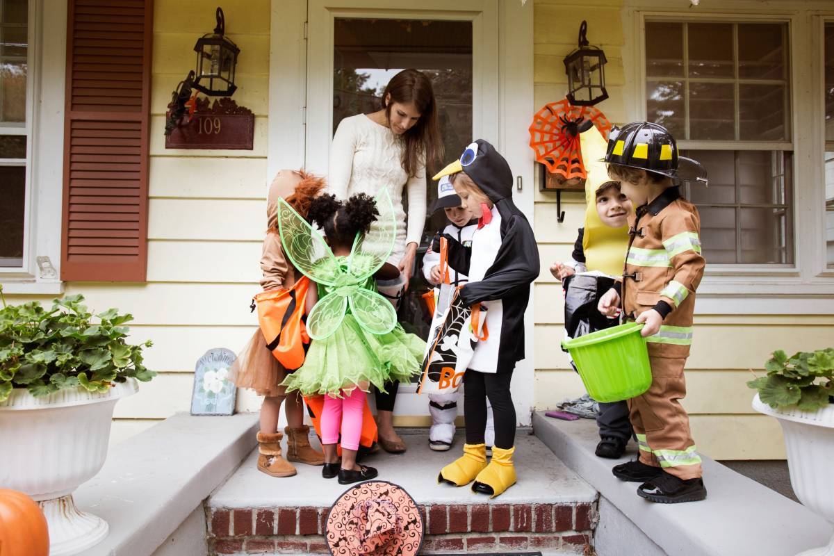 6 kids in Halloween costumes getting candy from a woman on her doorstep.