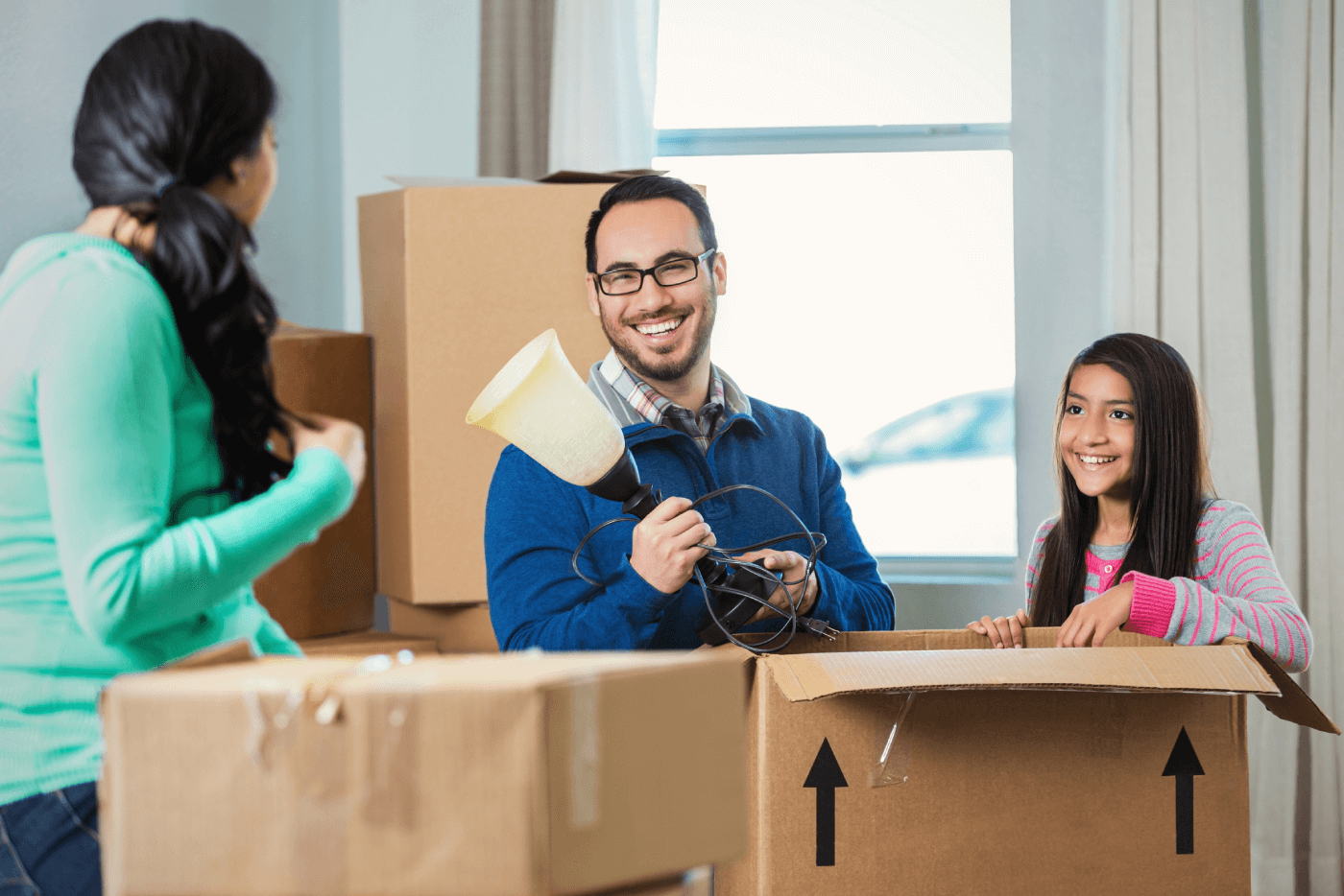 Padre sosteniendo una lámpara mientras hija y madre ayudan a empaquetar cajas de mudanza.