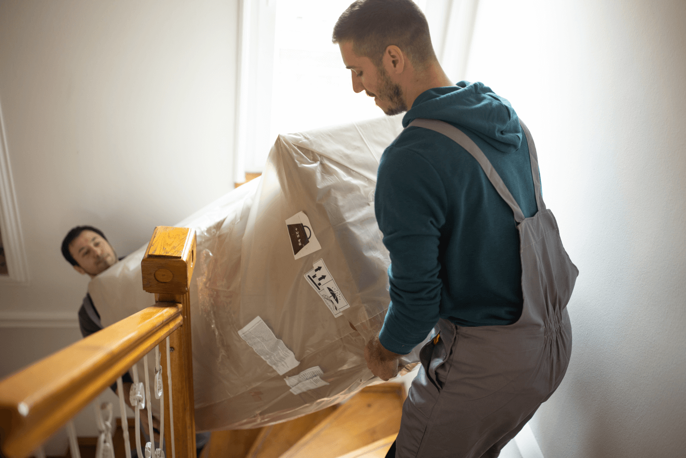 Dos empleados de una empresa de mudanzas suben un sofá por las escaleras de una casa.