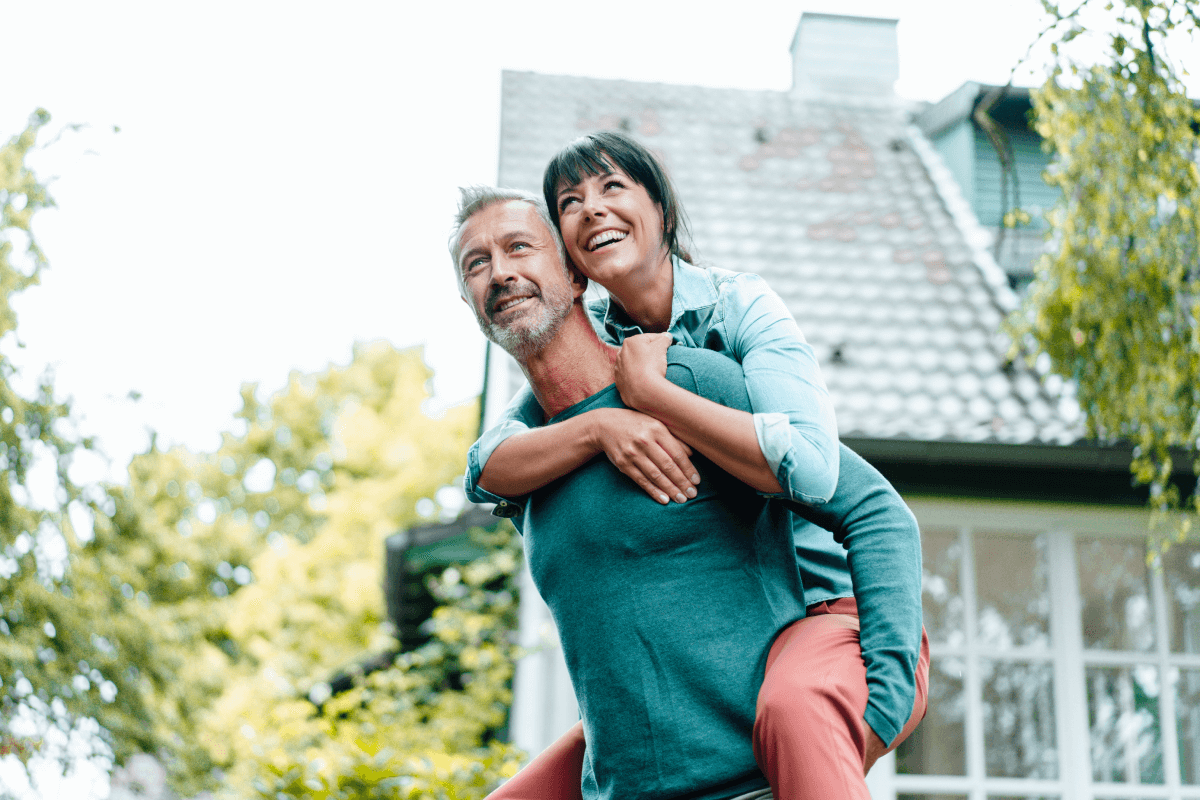 Happy middle aged couple. Man is holding woman on his back as they play in the yard.