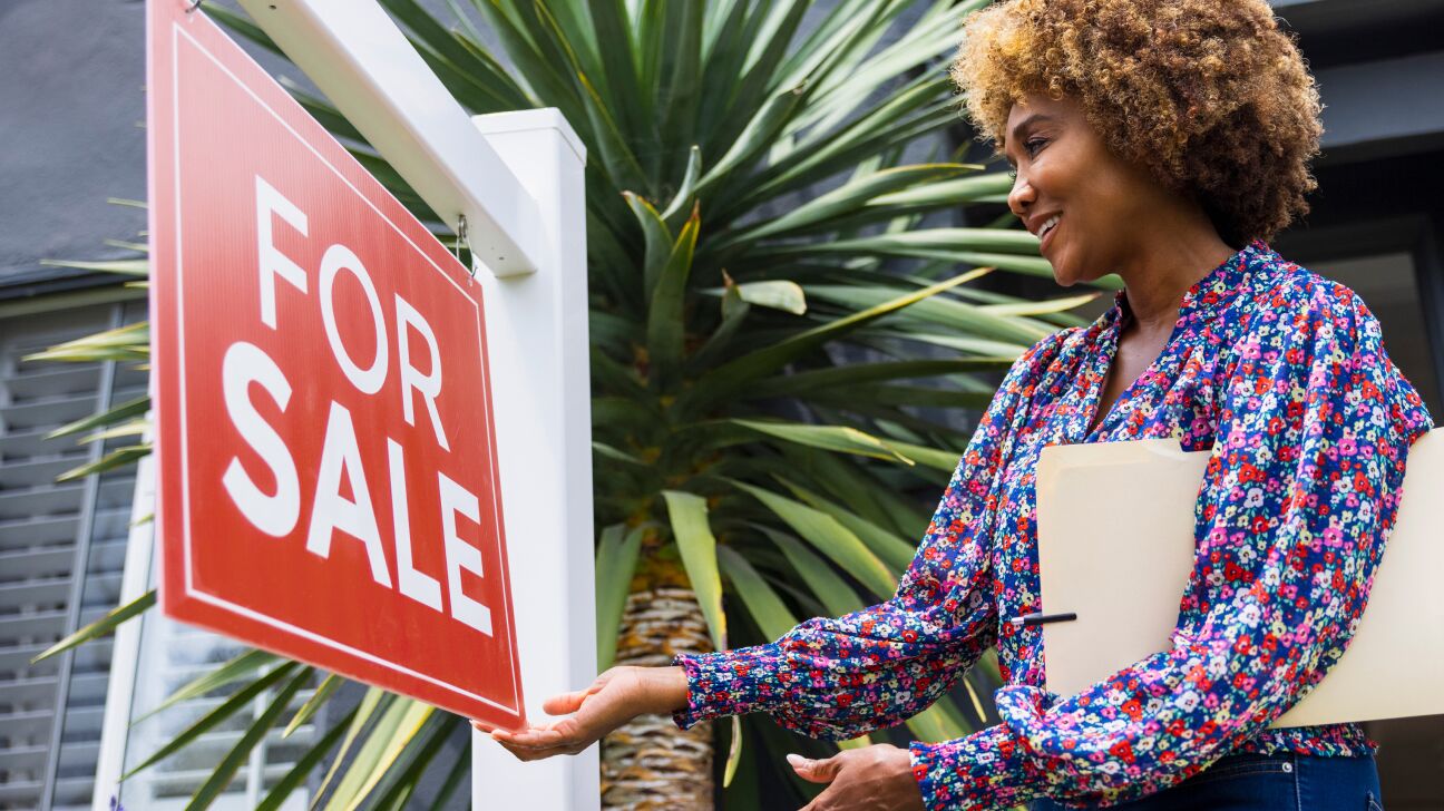 Realtor hanging a For Sale sign in front of a house.