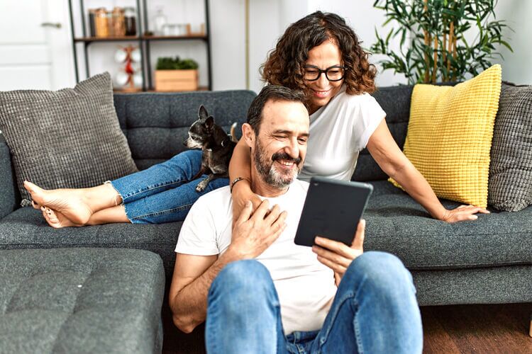 Un hombre, una mujer y un perro en un sofá mirando la pantalla de una tableta para comprar un plan legal LegalShield.