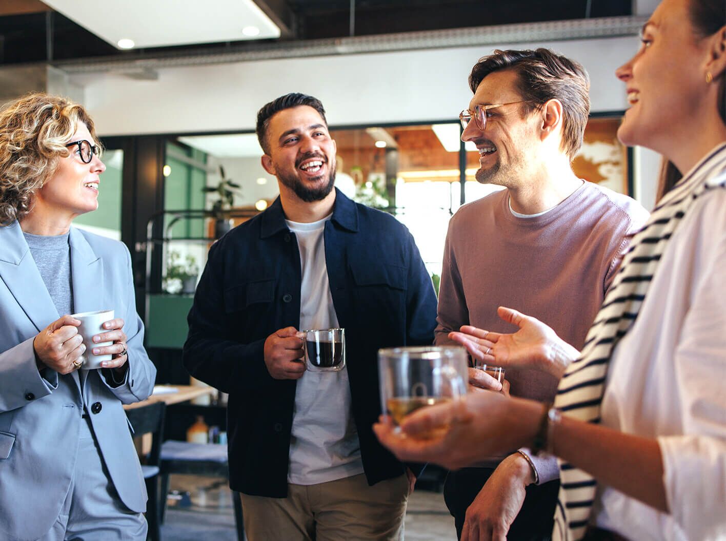 3 men and a business woman talking casually as they drink beverages.