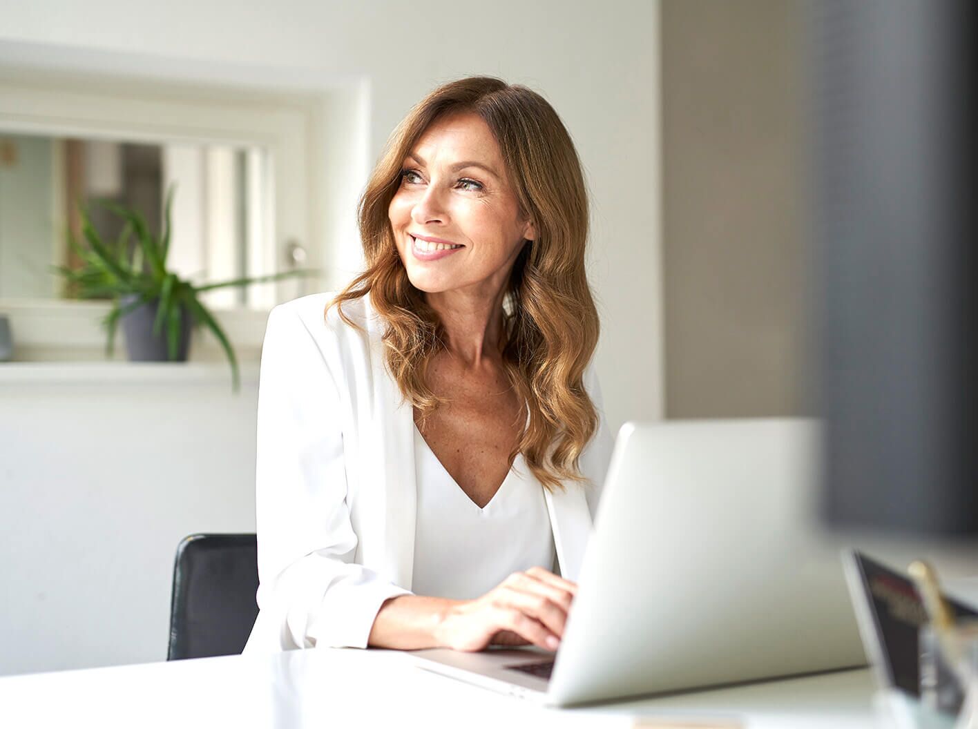 Smiling woman working on a laptop at an office desk.