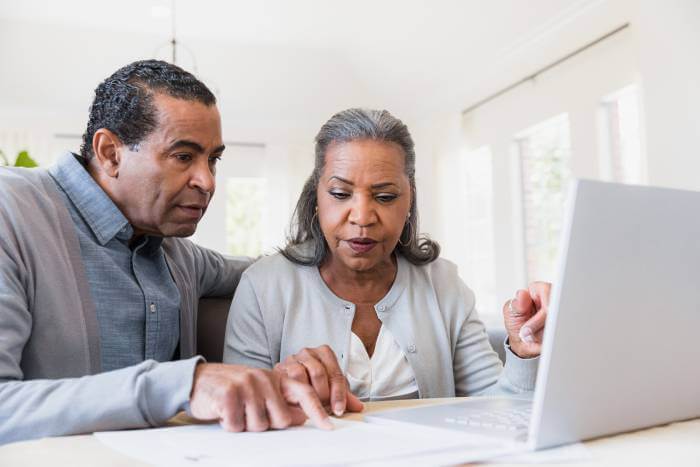 Pareja mirando documentos de jubilación sentada frente a un ordenador portátil.