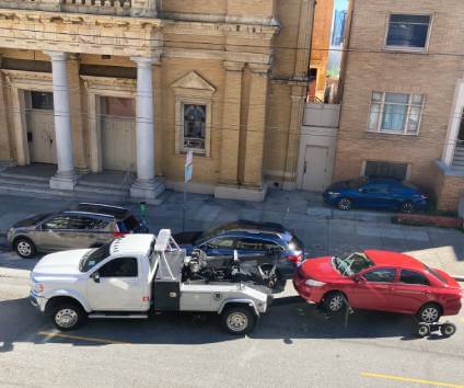 Tow truck taking away red car being repossessed.