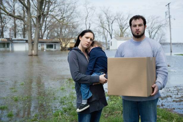 Mother, father and child standing next to rental home flooded by storm water and facing eviction.