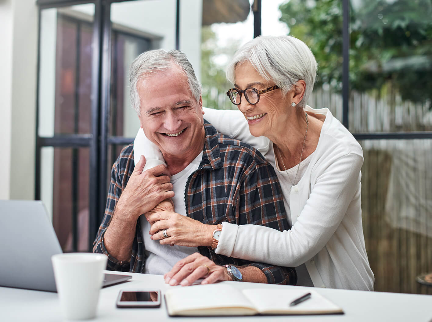 A woman sitting behind a man and wrapping her arms around him.