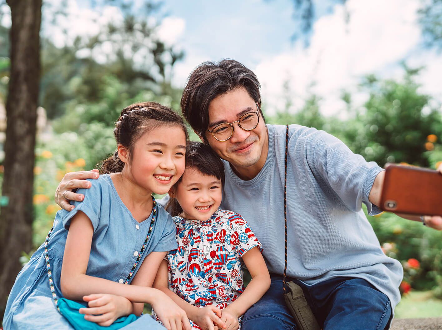 Father taking a selfie with his young son and daughter in the outdoors.