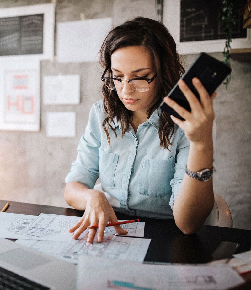 Mujer revisando documentos de negocios mientras sostiene su teléfono móvil.