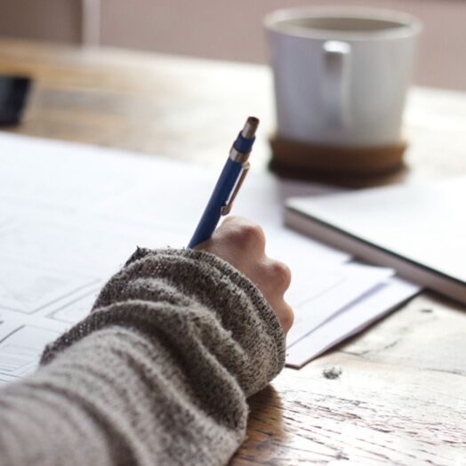 Mujer escribiendo en documentos en su escritorio junto a una taza de café.