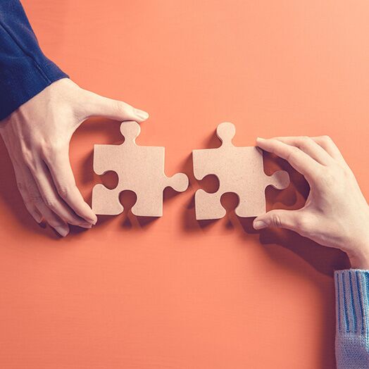 Dos piezas de puzzle empujadas juntas por la mano de una mujer y la de un hombre.