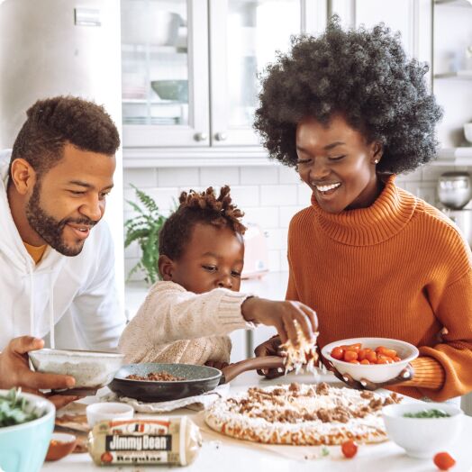 Madre, padre e hija pequeña preparando una pizza juntos en su cocina.