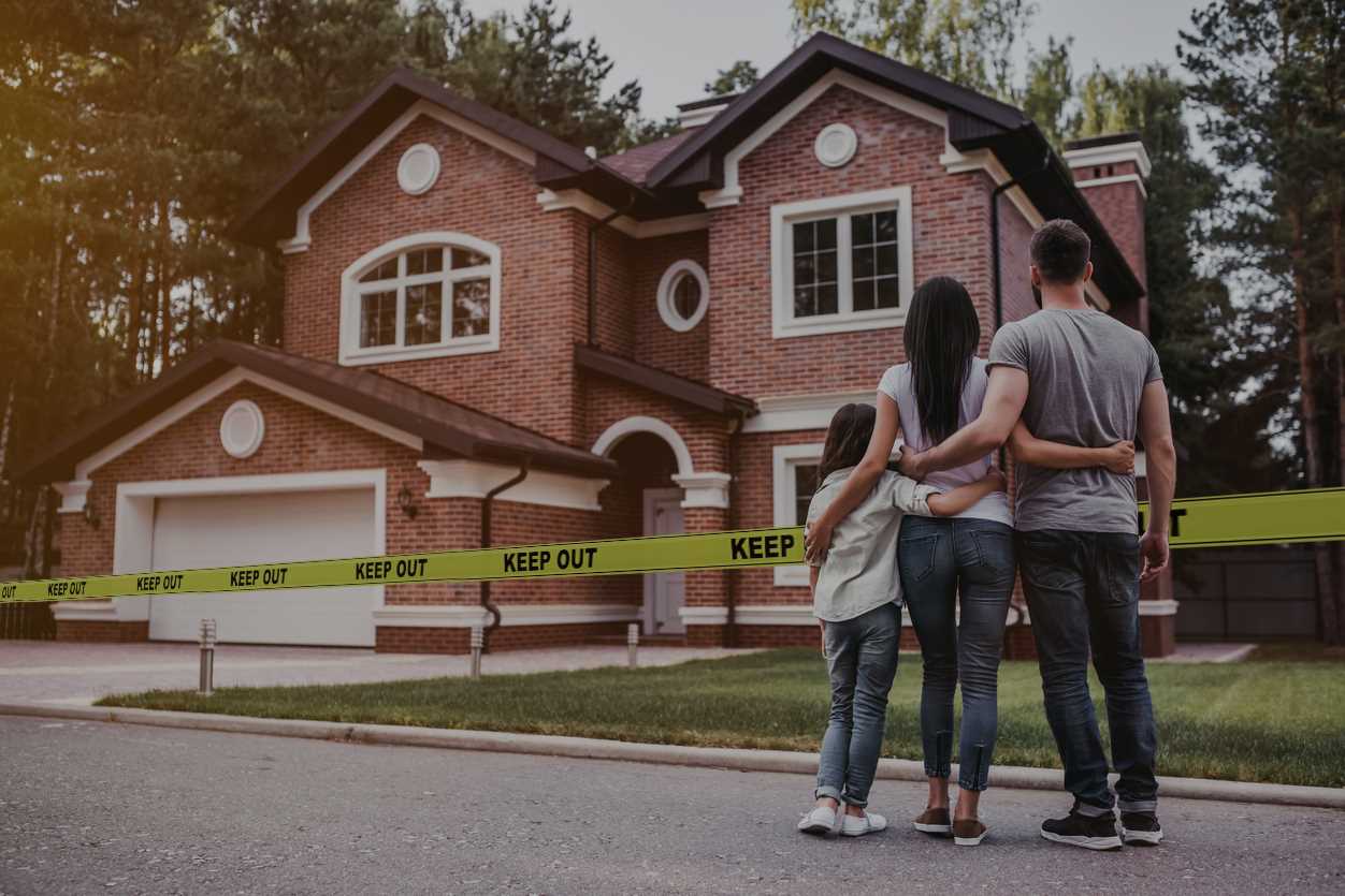 Parents and young daughter embracing while looking at 2-story brick home with Keep Out yellow tape around it