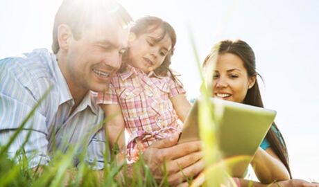 Young family laying on grass planning their summer vacation