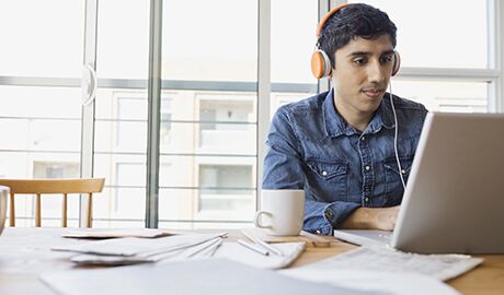 Estudiante universitario usando audífonos y trabajando en una computadora portátil