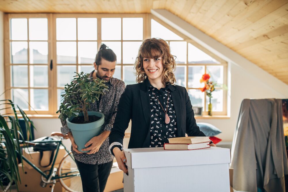 Couple carrying boxes and plant into new rental home