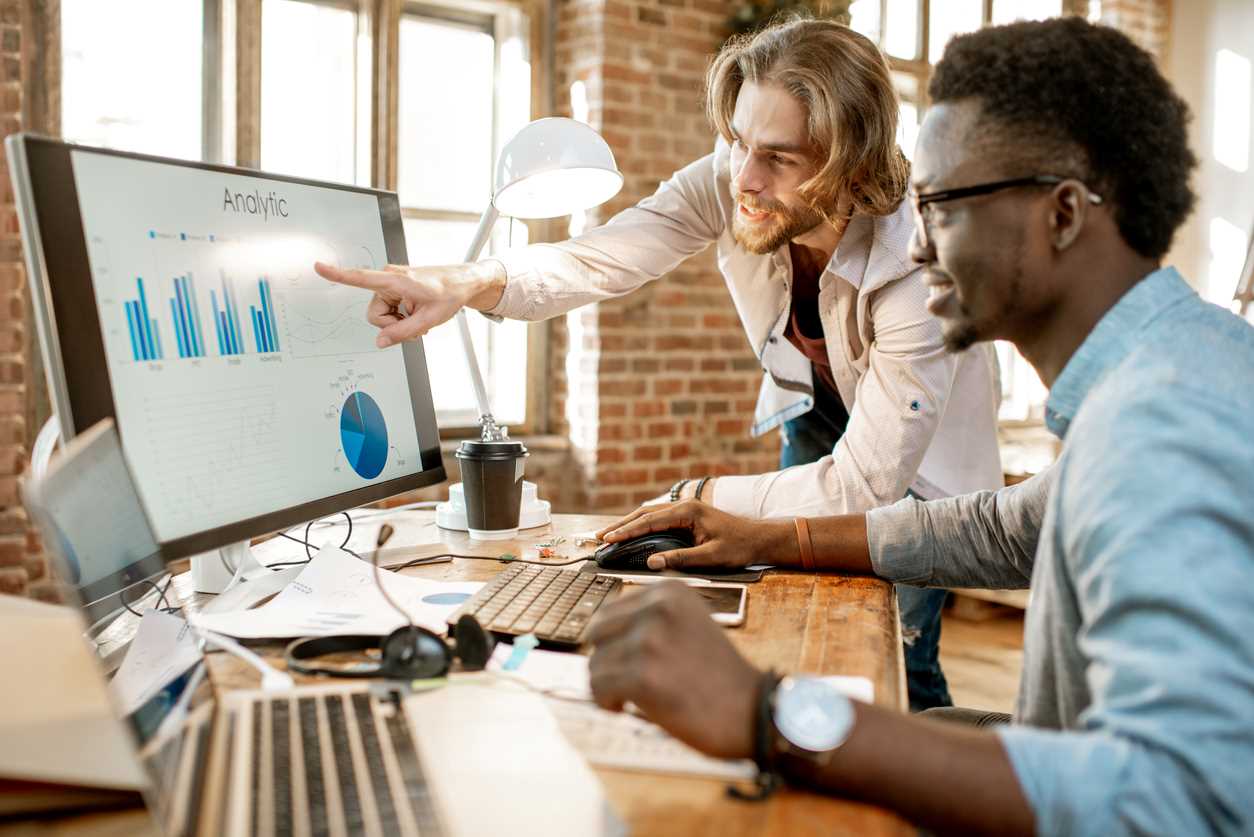 Dos compañeros de trabajo mirando análisis de sitios web de negocios en el monitor de la computadora