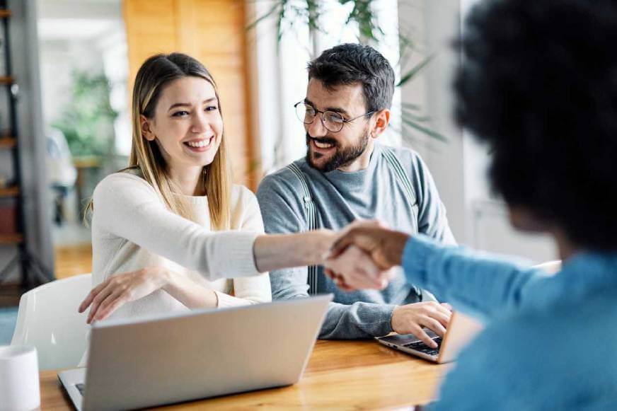 Young woman sitting next to her husband is shaking the hand of her female LegalShield provider lawyer who is drafting her Last Will and Testament..