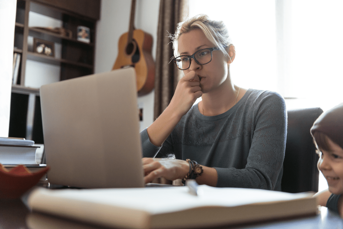 Woman working on laptop with young son nearby.