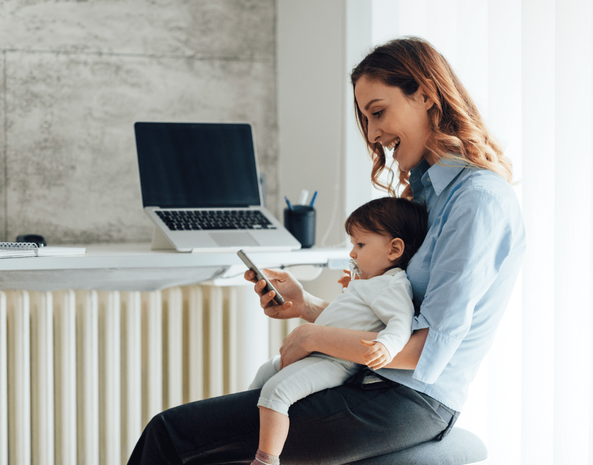 Mother holding her child as she looks at mobile phone and smiles.