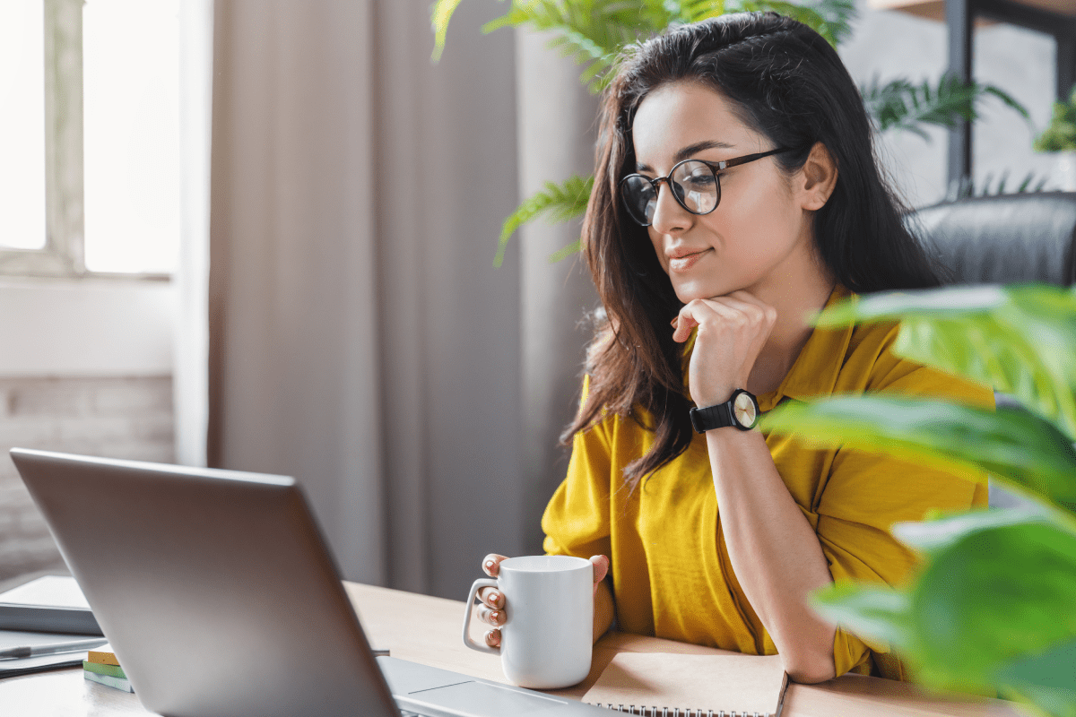 Woman looking at laptop and holding a coffee cup