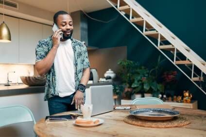 Man working to file his taxes online while in his kitchen and talking on the phone.