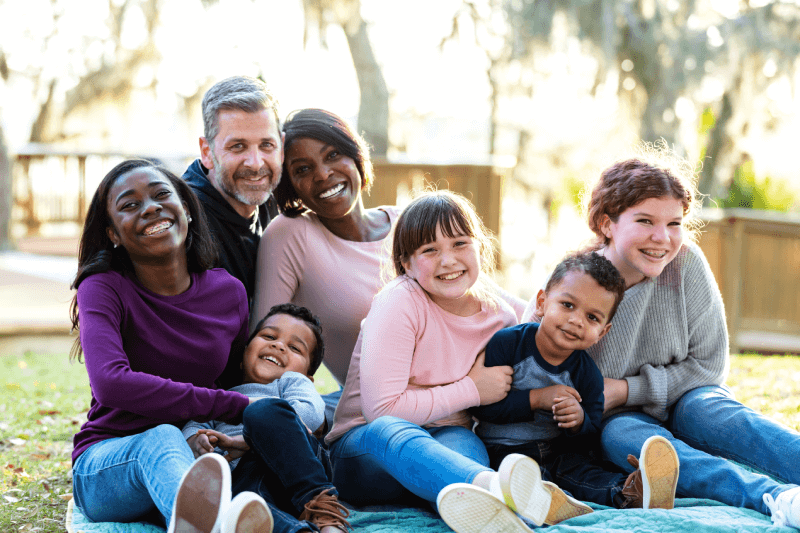 Una familia mezclada de 7 personas sentadas en el suelo para un retrato.