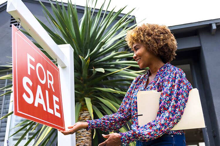 Woman adjusting the for sale sign outside of a house