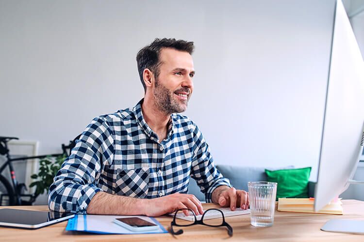 Man sitting in front of a computer monitor and smiling.